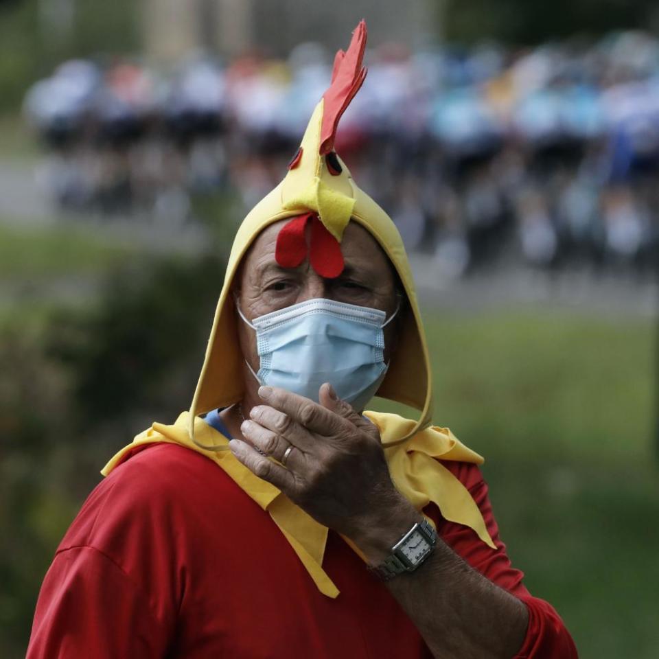 A spectator dressed up as a rooster wearing a mask stands along the road of the ninth stage from Pau to Larun.