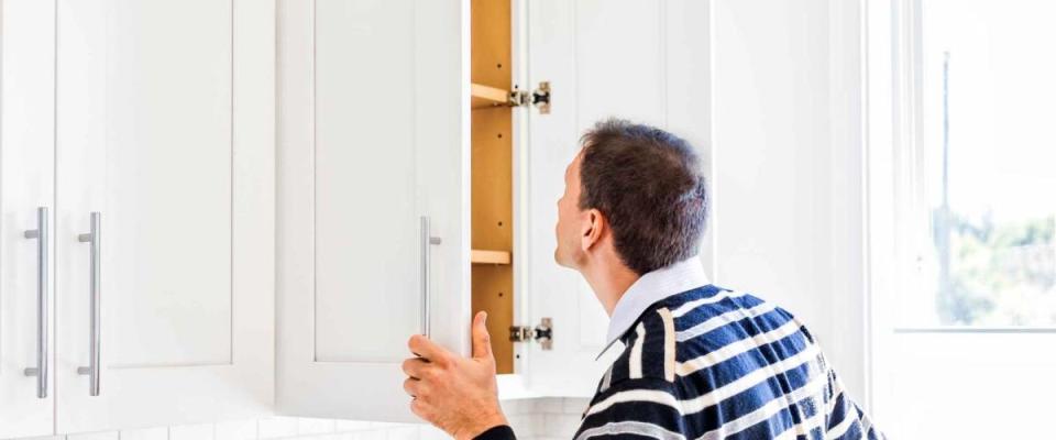 Young man checking looking inside empty kitchen modern cabinets by window after or before moving in