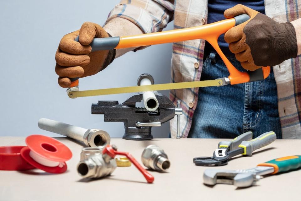 A diy plumber using a hacksaw to cut PVC pipe for a plumbing repair.