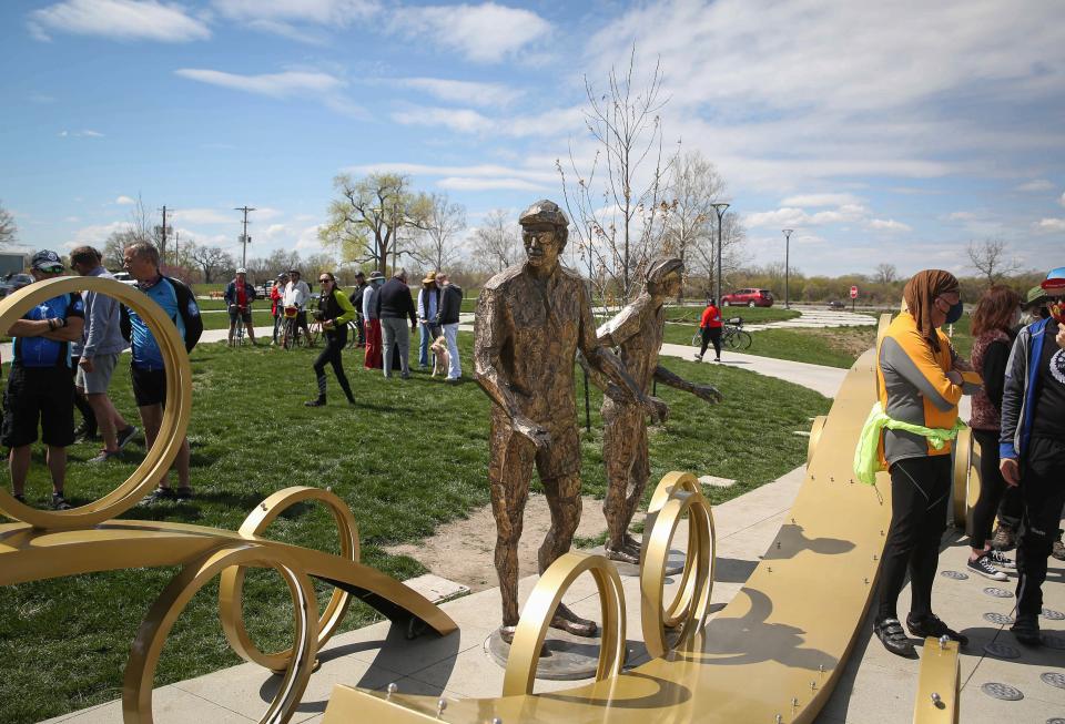 Cycling enthusiasts gather following a bike ride on April 17, 2021, at Water Works Park in Des Moines for the public dedication of the Founder's Statue, a life-sized depicition of John Karras and Donald Kaul, the founders of RAGBRAI, on their inaugural 1973 ride.