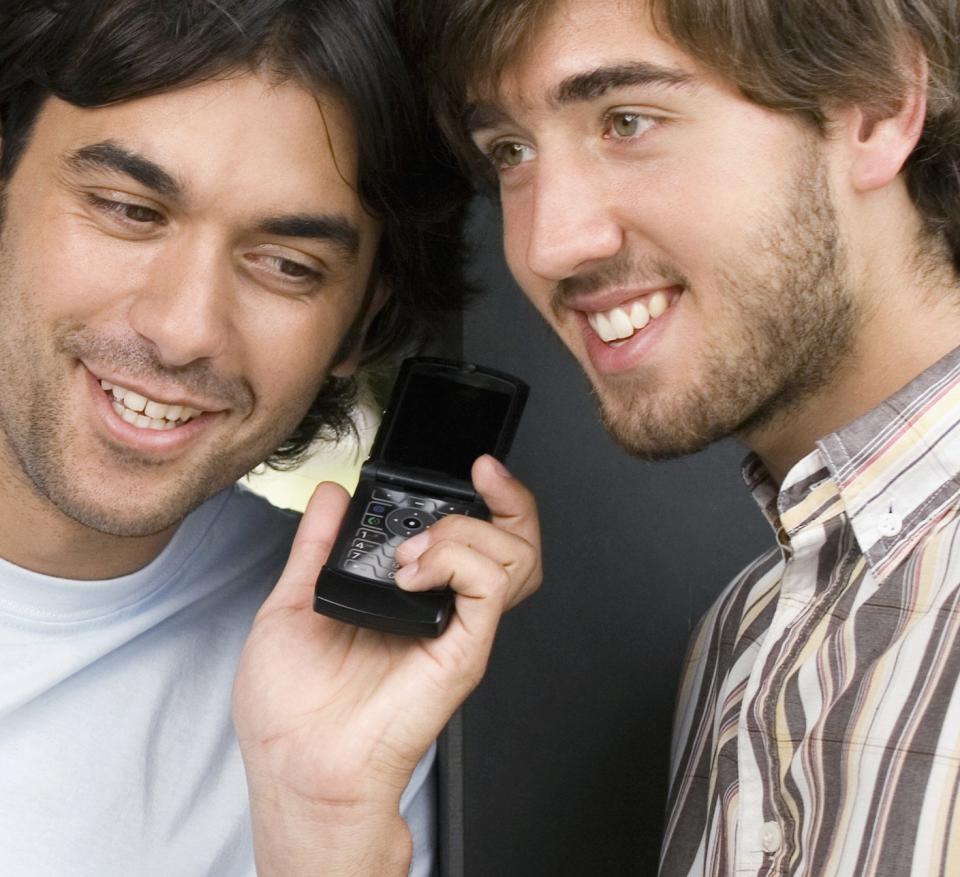 Two guys listening on to a phone in between both of them