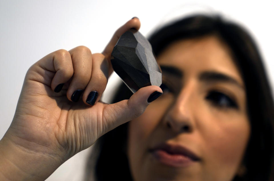 An employee of Sotheby's Dubai presents a 555.55 Carat Black Diamond "The Enigma" to be auctioned at Sotheby's Dubai gallery, in Dubai, United Arab Emirates, Monday, Jan. 17, 2022. (AP Photo/Kamran Jebreili)