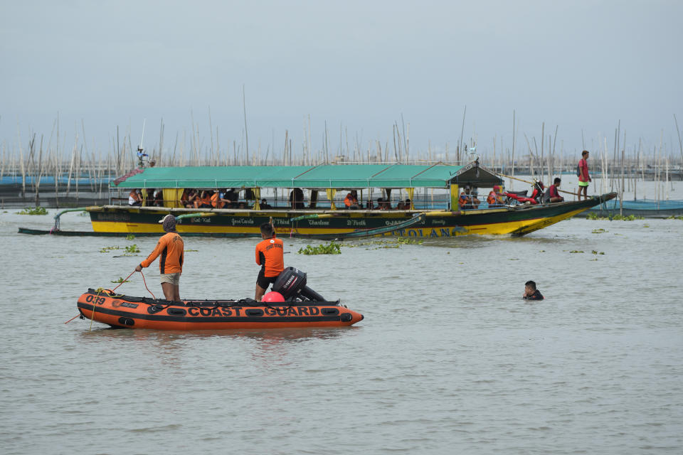 Rescuers search for victims of a capsized ferry as a passenger boat cruises nearby in Binangonan, Rizal province, Philippines, Friday, July 28, 2023. A boat turned upside down on Thursday when passengers suddenly crowded to one side in panic as fierce winds pummeled the wooden vessel, killing a number of people, officials said Friday. (AP Photo/Aaron Favila)