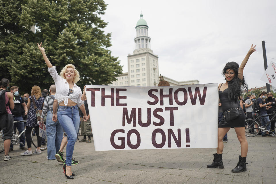 Suzy and Rachel, two performers from the Estrel Hotel looking like Marilyn Monroe and Amy Winehouse, hold a poster with the words "The Show must go on!" during a demonstration of the event industry in Berlin, Germany, Friday, July 10, 2020. With their second protest march, Berlin venues, event organisers, technicians, stage and stand builders and other service providers from the culture and event industry once again remind people of their precarious situation and the lack of prospects due to the restrictions on their activities to contain the Corona pandemic. (Joerg Carstensen/dpa via AP)