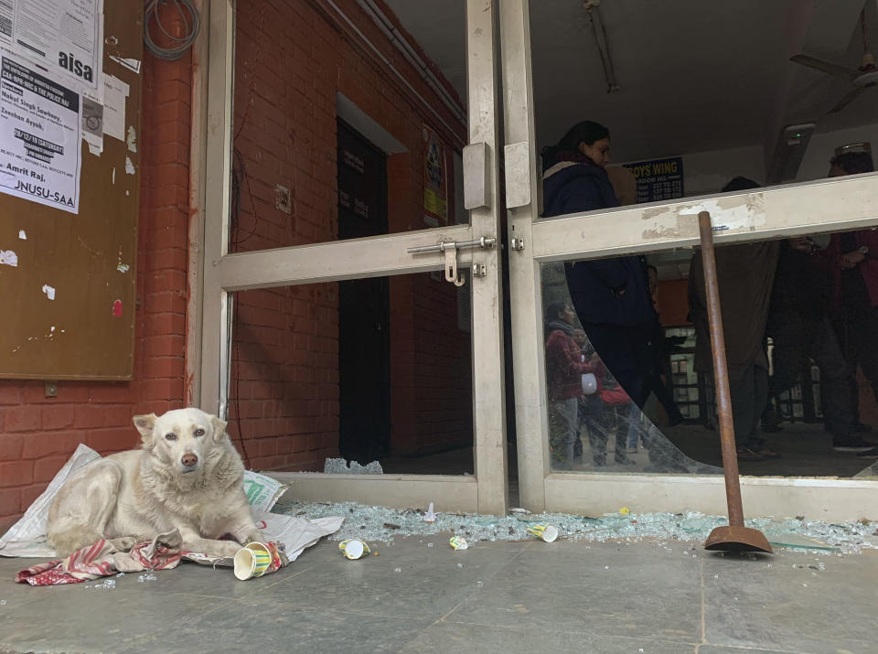 A dog rests next to shattered glass of a student hostel building after Sunday's assault by masked assailants at the Jawaharlal Nehru University in New Delhi, India, Monday, Jan. 6, 2020. More than 20 people were injured in the attack opposition lawmakers are trying to link to the government. (AP Photo/Emily Schmall)