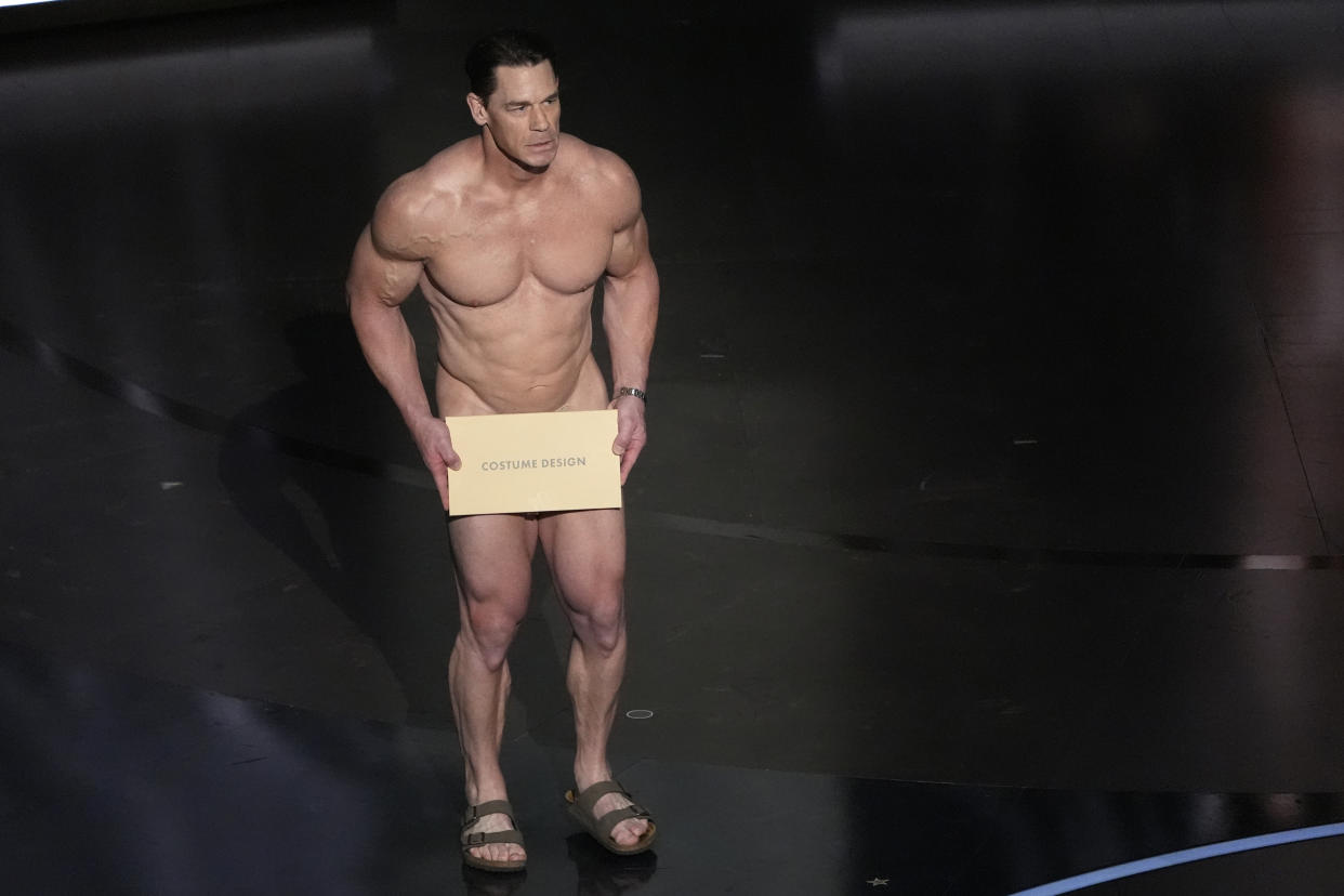 John Cena, seeming naked except for sandals and a large card he holds in front of his private parts, presents the award for best costume design.