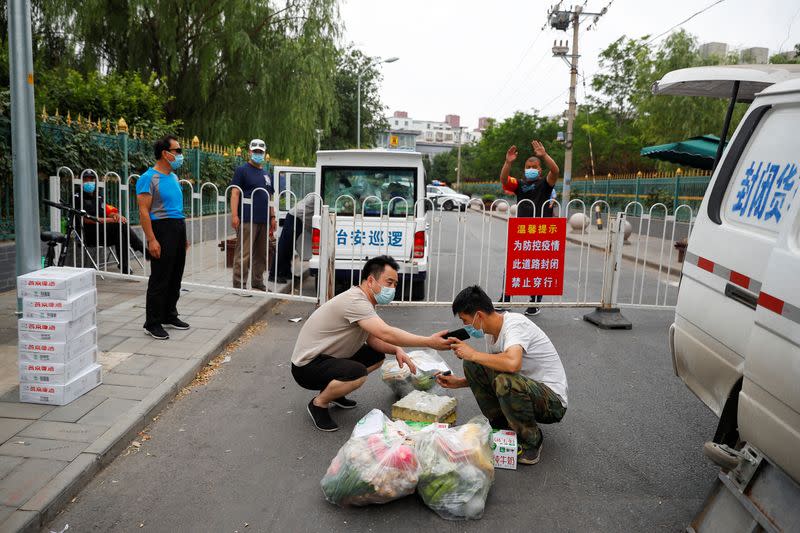 People deliver food across a barrier near a residential compound that is under lockdown in the Fengtai district, in Beijing
