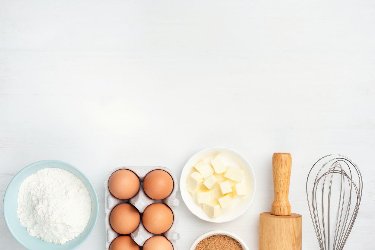 Baking ingredients and kitchen utensils on white background. Chicken eggs, butter, sugar, flour, rolling pin and whisker. Cooking, baking, pastry or cookie dough ingredients