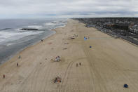 FILE - In this May 23, 2020, file photo visitors walk down the boardwalk, right, beside a mostly empty beach in Belmar, N.J., during the coronavirus outbreak. As some parts of the nation continue to ease stay-at-home orders meant to slow the spread of the coronavirus, the economy remains in free fall. President Donald Trump says that the country is anxious to get back to work and that pent-up consumer demand can turn things around quickly. Presumptive Democratic nominee Joe Biden counters by urging caution and heeding medical and scientific experts. (AP Photo/John Minchillo, File)