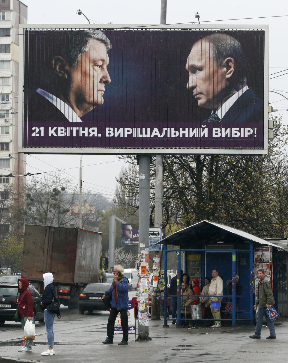 People pass by a billboard depicting Ukraine's President Petro Poroshenko and Russian President Vladimir Putin looking at each other in Kiev, Ukraine, Thursday, April 11, 2019. Writing on the big board reads: "A decisive choice." Poroshenko is running for his second term at the second round of presidential vote on April 21. He advocates Ukraine's integration into the European Union back from Russian influence. (AP Photo/Efrem Lukatsky)