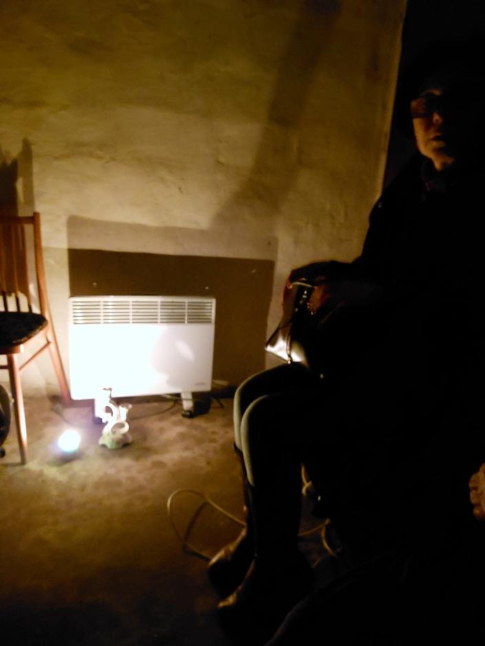 woman sits on chair in dark basement with a light on the floor