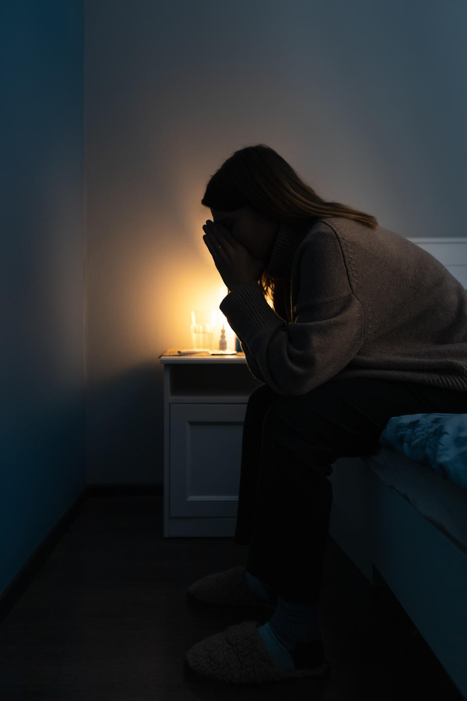 A woman sitting on the edge of her bed in the dark