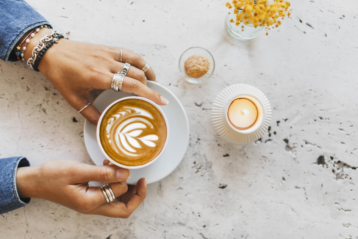 Frauenhände an Tasse mit Kaffee und Milchschaum, der aussieht wie ein Blatt und ein Herz