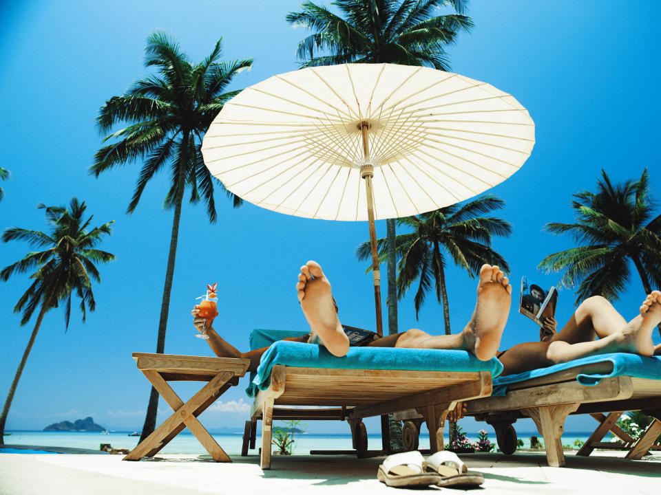 Two people relaxing on sun loungers under a large umbrella, tropical beach setting