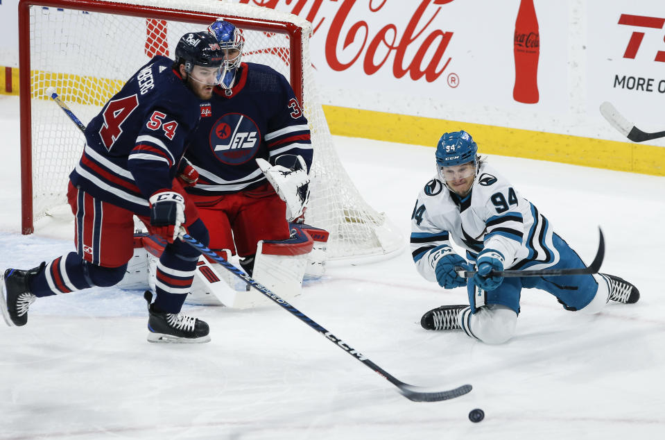 Winnipeg Jets' Dylan Samberg (54) and San Jose Sharks' Alexander Barabanov (94) reach for the puck during the first period of an NHL hockey game Wednesday, Feb. 14, 2024, in Winnipeg, Manitoba. (John Woods/The Canadian Press via AP)