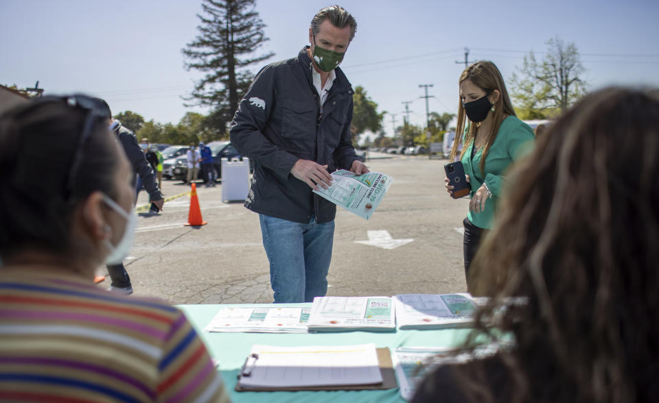 California Gov. Gavin Newsom, left, grabs a flyer as Tiburcio Vasquez Health Center CEO Andrea Schwab-Galindo, right, looks on during a visit with staff members at the health center's vaccination site at Our Lady of the Rosary church in Union City, Calif., on Thursday, April 15, 2021. The state expanded vaccine eligibility to all Californians aged 16 and older on Thursday. (Anda Chu/Bay Area News Group via AP)