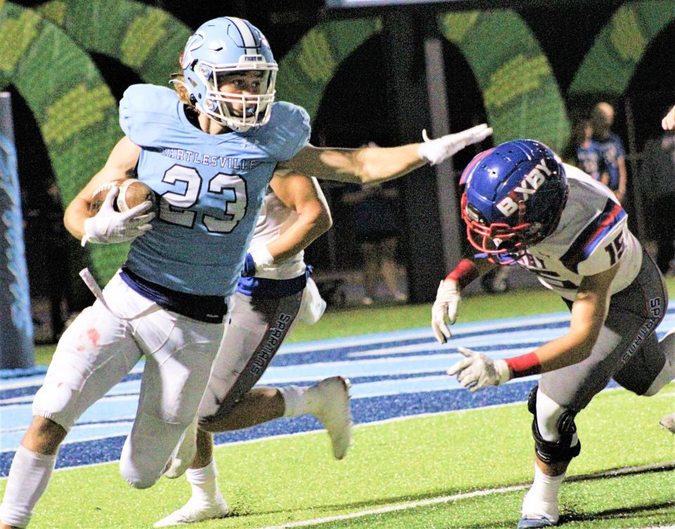 Bartlesville High's Gage Keaton, left, looks to carve out some more yards by holding off a would-be Bixby High tackler by arm's length.