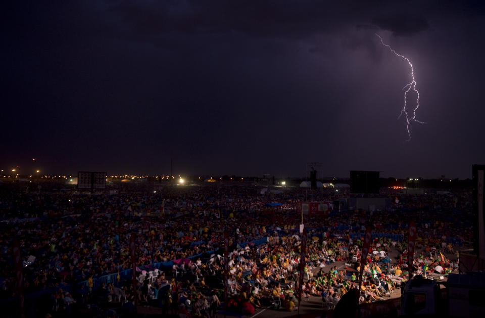 FILE - Lightning illuminates the sky as pilgrims look at a screen showing Pope Benedict XVI in Cuatro Vientos, near to Madrid, Spain, on Aug. 20, 2011. He was the reluctant pope, a shy bookworm who preferred solitary walks in the Alps and Mozart piano concertos to the public glare and majesty of Vatican pageantry. When Cardinal Joseph Ratzinger became Pope Benedict XVI and was thrust into the footsteps of his beloved and charismatic predecessor, he said he felt a guillotine had come down on him. The Vatican announced Saturday Dec. 31, 2022 that Benedict, the former Joseph Ratzinger, had died at age 95. (AP Photo/Alvaro Barrientos, File)