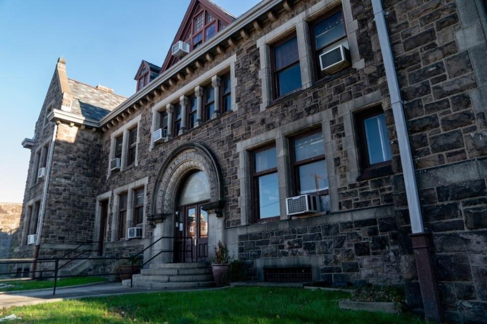 A stone building with large windows, air conditioners, and an arched entrance. There's a ramp and steps leading to the door