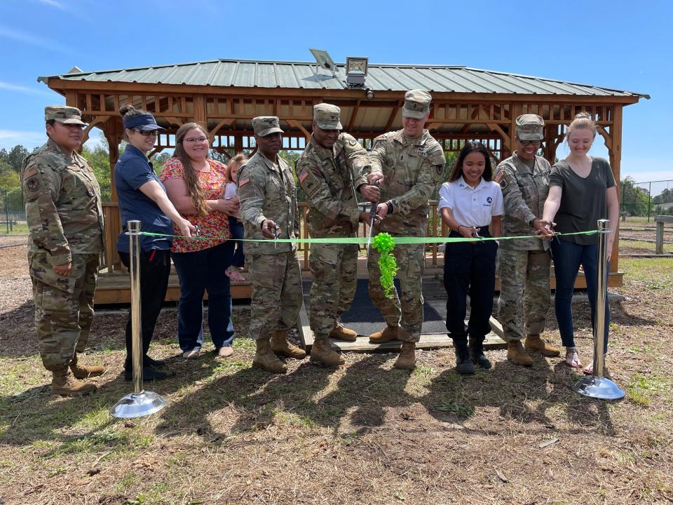 Wielding an oversized pair of scissors, Fort Gordon Garrison Commander Col. Reginald Evans (center) and Command Sgt. Maj. Aaron Rose (fourth from right) cut the ribbon on the fort's reopened community garden, March 29, 2023.