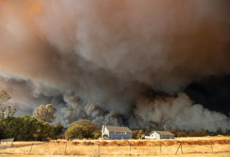 In this photo taken on November 8, 2018 a home is overshadowed by towering smoke plumes as the Camp fire races through town in Paradise, California