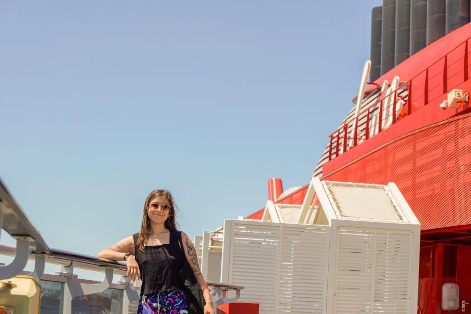 The author leans against the side of a cruise ship with blue skies behind her.