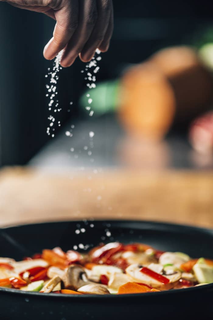 Sprinkling salt on top of sautéed vegetables.