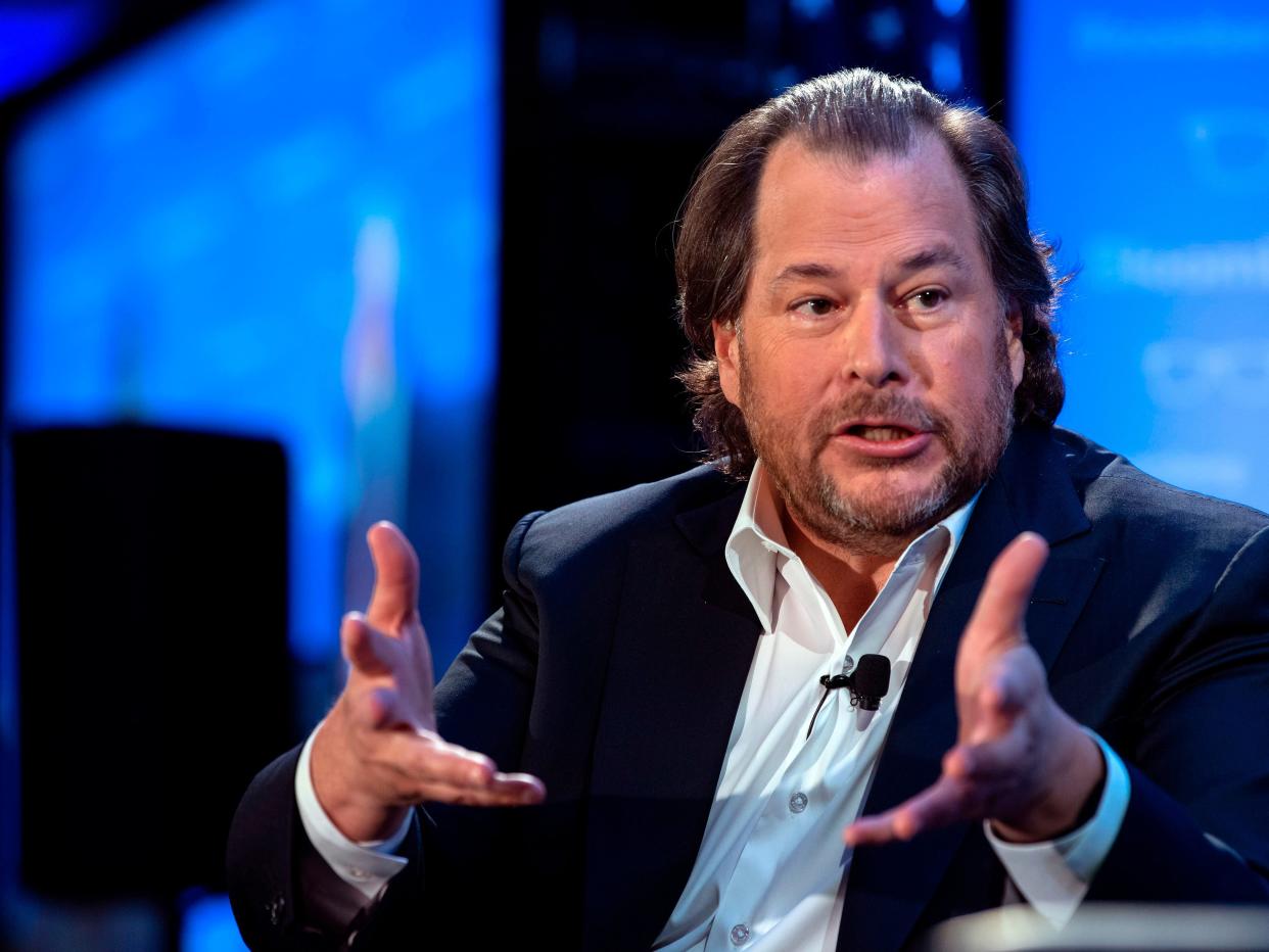 Salesforce founder Marc Benioff, wearing a sports coat jacket and in front of a blue background on a stage, extends his hands forward during a talk.