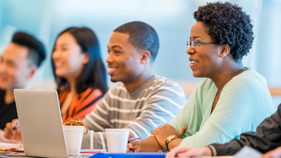 A multi-ethnic group of college students are sitting in a lecture hall and are working on a homework assignment for a group project.