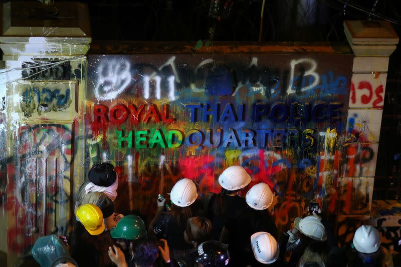 Demonstrators spray-paint the plaque with lettering on it in front of the police headquarters during a rally in Bangkok