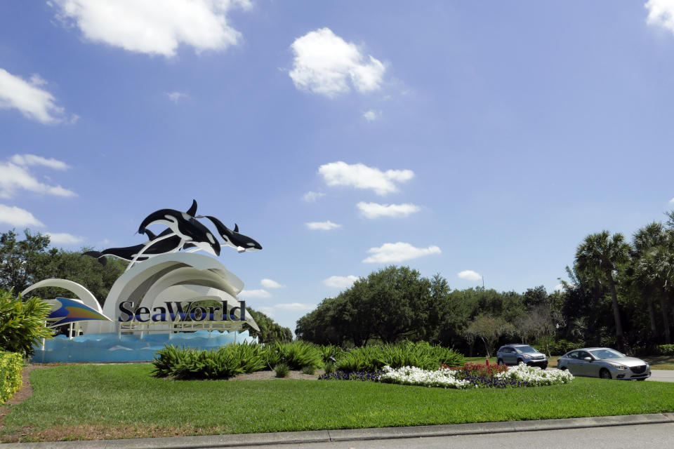 Cars pass by the entrance to the SeaWorld Theme park as it remains closed Monday, March 30, 2020, in Orlando, Fla. SeaWorld is indefinitely furloughing more than 90% of its employees and they won't get paid after March 31. (AP Photo/John Raoux)
