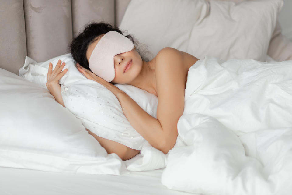 Beautiful woman sleeping seeing dreams wearing sleep mask in comfortable bed lying on soft white pillow orthopedic mattress under duvet blanket on white sheets in bedroom. Good night