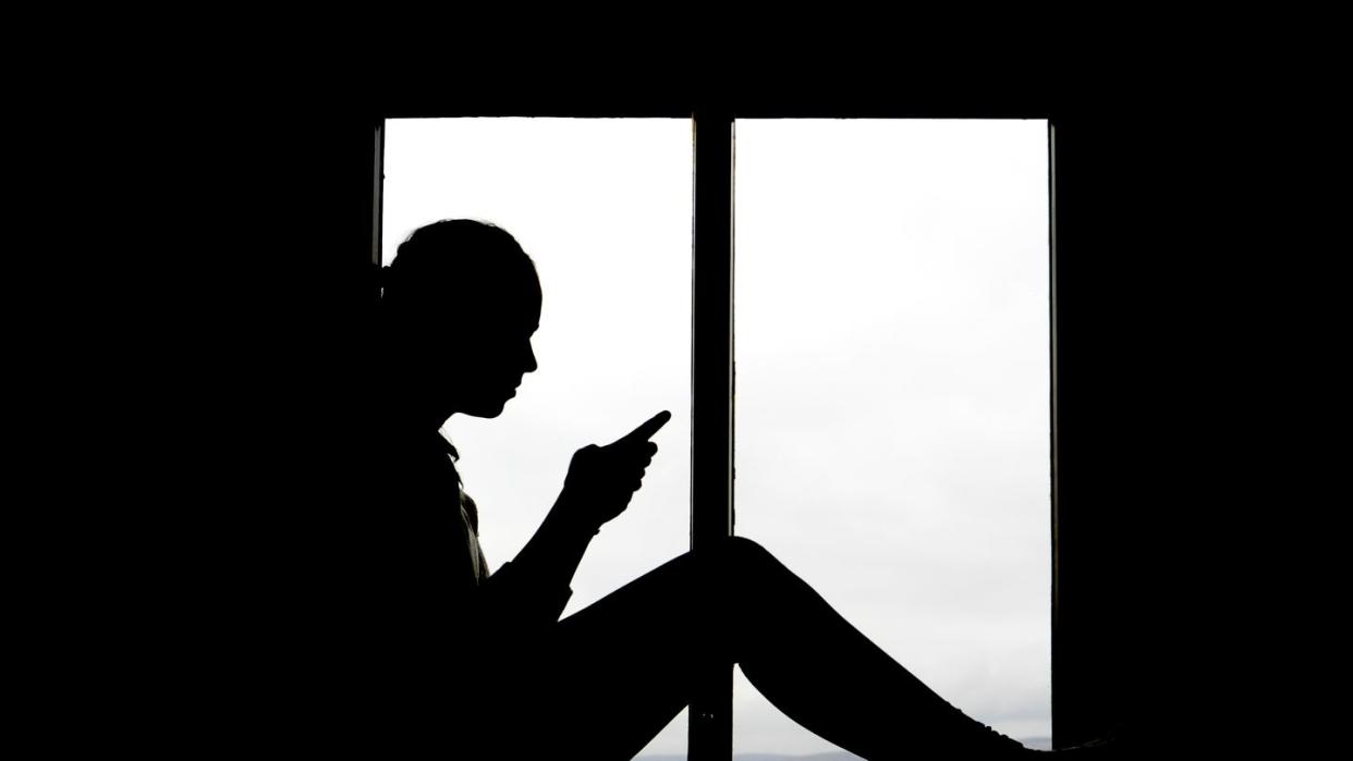 silhouette of 16 year old girl texting backlit at window