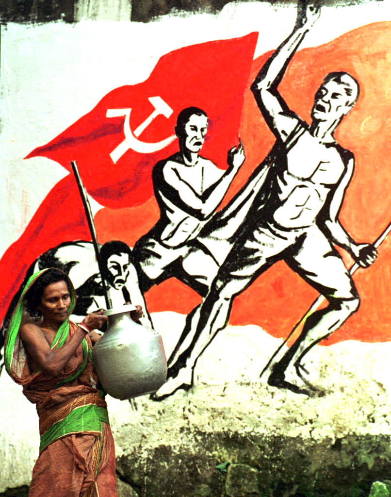 A woman carrying drinking water collected from a road-side well, walks past a wall mural 09 October in Calcutta, painted to mark the 16th party congress of the Communist Party of India-Marxist [CPI(M)] being held in the city. Colourful wall murals and banners have flooded the city for the week long party congress of CPI(M) which concludes 11 October.<br>AFP PHOTO