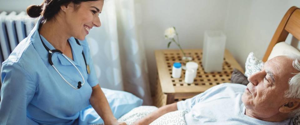 Nurse holding hands of senior man in bedroom