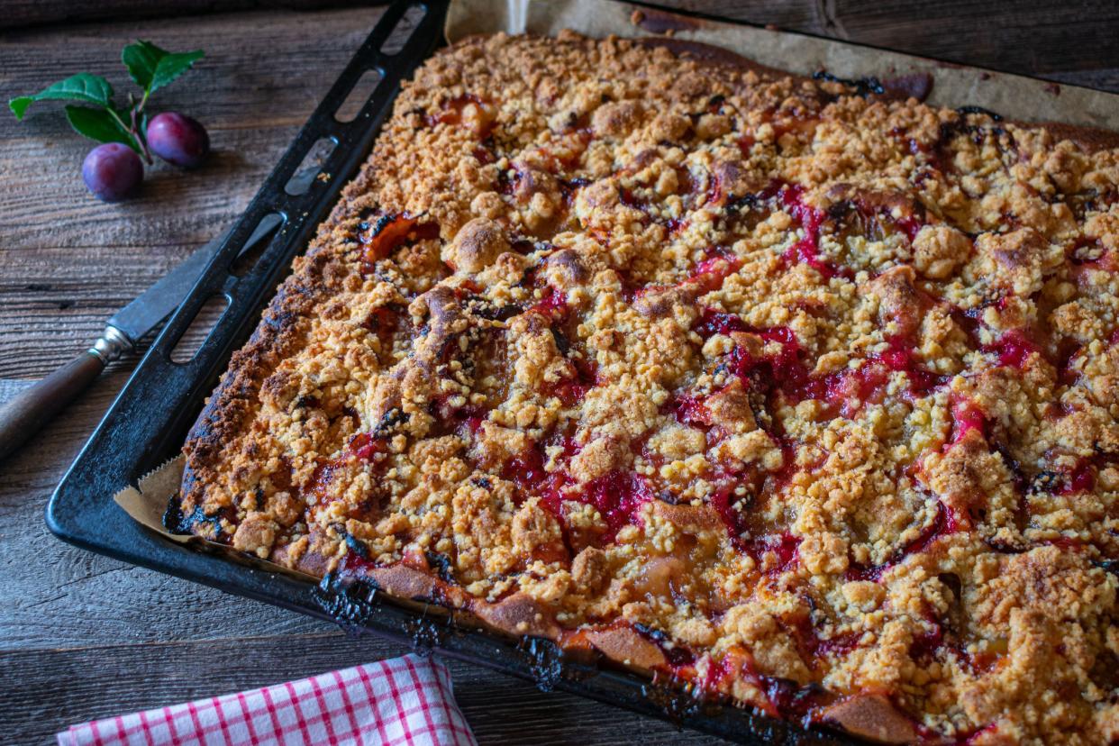 Fresh and homemade baked traditional plum crumble cake from Germany. Served on a baking tray on rustic and wooden table background.