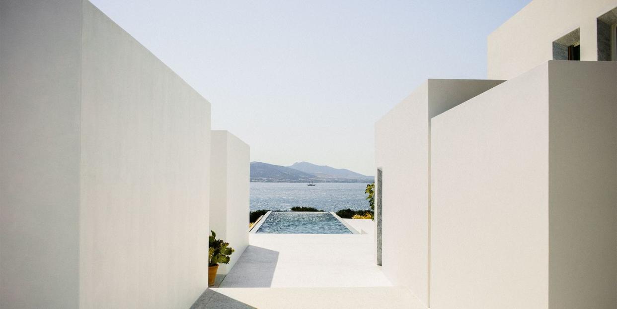 concrete walls on either side lead to the rectangular pool which juts out and overlooks bushes and the sea and mountains beyond