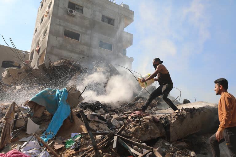 Palestinos sofocan las llamas sobre los escombros de edificios destruidos por el bombardeo israelí de la Franja de Gaza en el campamento de refugiados Nusseirat, 17 de noviembre de 2023. (AP Foto/Marwan Saleh)