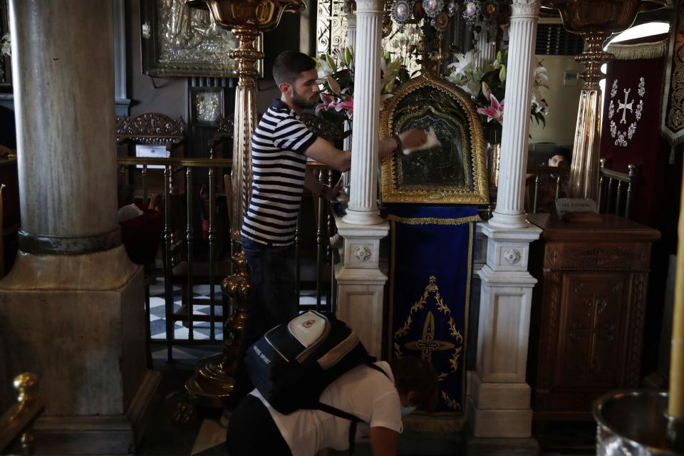 A worker cleans an icon believed to perform miracles as a pilgrim crawls inside the Holy Church of Panagia of Tinos, on the Aegean island of Tinos, Greece, on Thursday, Aug. 13, 2020. For nearly 200 years, Greek Orthodox faithful have flocked to Tinos for the August 15 feast day of the Assumption of the Virgin Mary, the most revered religious holiday in the Orthodox calendar after Easter. But this year there was no procession, the ceremony _ like so many lives across the globe _ upended by the coronavirus pandemic. (AP Photo/Thanassis Stavrakis)