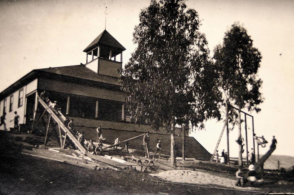 Children play at the Avila school house while workmen at left pose for the picture in this undated image. This Avila Beach school was built in 1912.