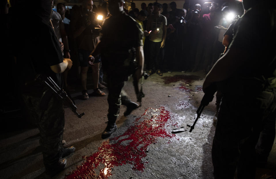 Palestinian Hamas masked gunmen stand guard around blood on the ground following an explosion targeted a Hamas police checkpoint in Gaza City, Tuesday, Aug. 27, 2019. (AP Photo/Khalil Hamra)