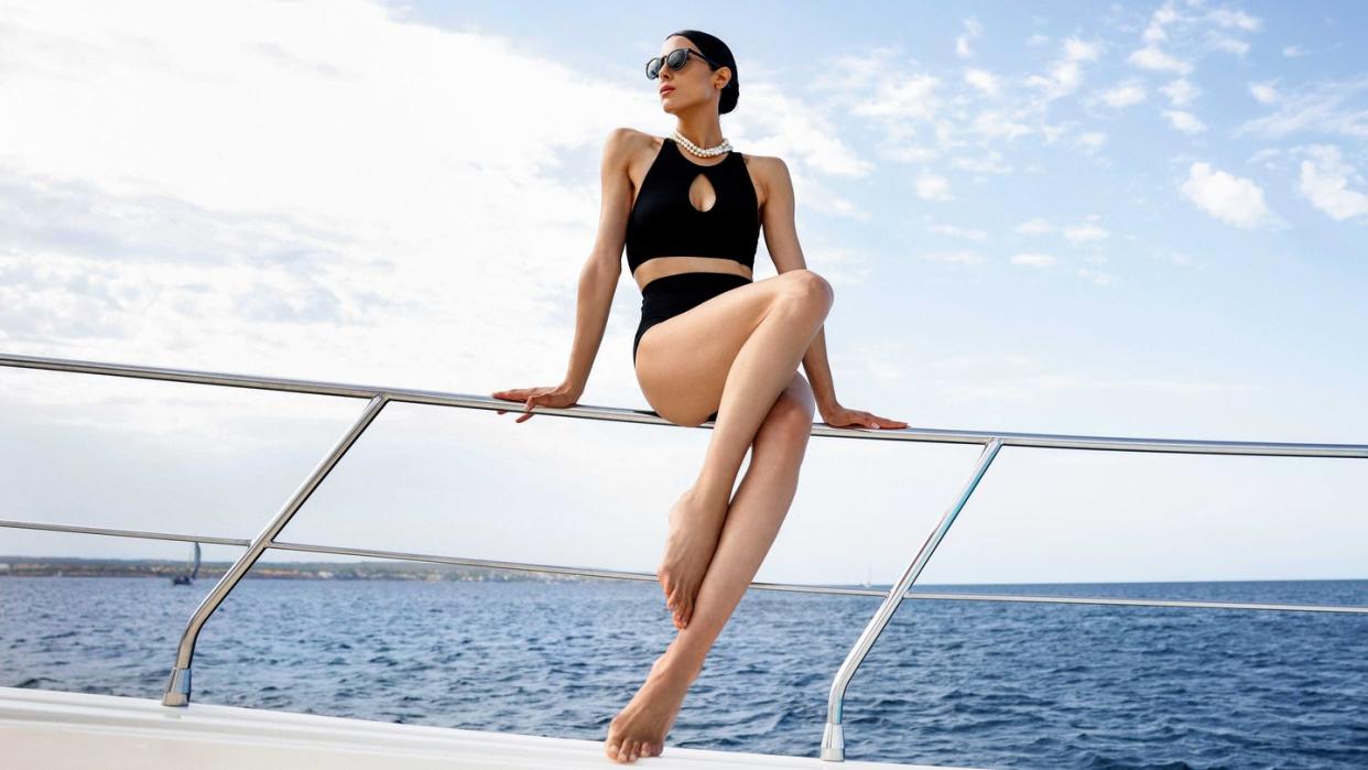 woman sitting on the edge of a boat railing wearing a black halter bikini, sunglasses, and a necklace