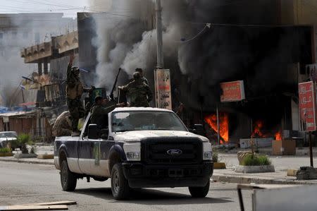 Members of Hashid Shaabi forces ride in a vehicle as smoke rises in shops at al-Qadisiya neighborhood, north of Tikrit April 3, 2015. REUTERS/Stringer