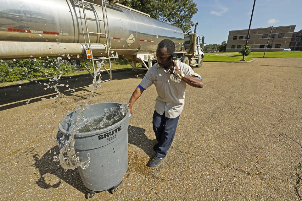 Santonia Matthews, a custodian at Forest Hill High School in Jackson, Miss., hauls away a trash can filled with water from a tanker in the school's parking lot, Wednesday, Aug. 31, 2022. The tanker is one of two placed strategically in the city to provide residents non-potable water. The recent flood worsened Jackson's longstanding water system problems and the state Health Department has had Mississippi's capital city under a boil-water notice since late July. (AP Photo/Rogelio V. Solis)