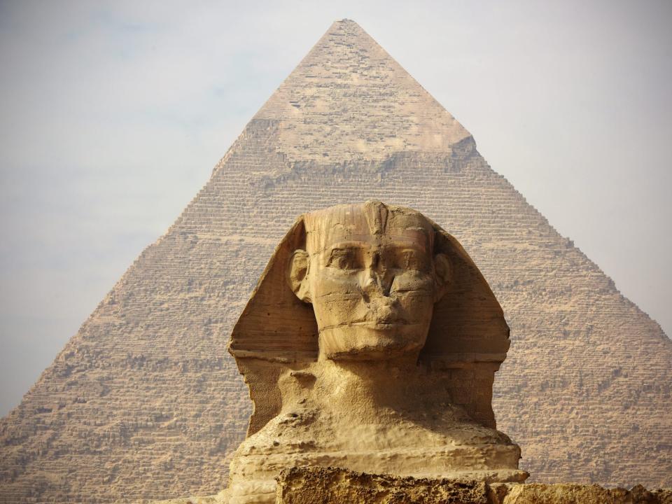 The sphinx is shown in fron of the pyramid which towers over it.