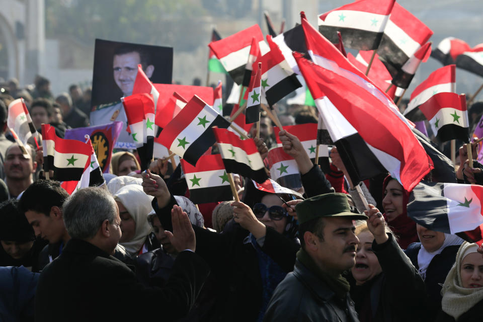 Pro-government supporters hold up the national Syrian flag and pictures of Syrian President Bashar Assad at a gathering at Saadallah al-Jabiri Square in Aleppo, Syria, Thursday, Jan. 19, 2017. Shells slammed into the northern Syrian city of Aleppo Thursday as thousands of government supporters gathered in the main square to celebrate last month's capture of the whole city by the army leading to a disperse by the gathering. (AP Photo/Hassan Ammar)