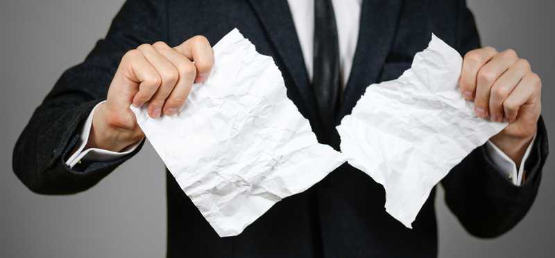 man in business suit tearing piece of paper in half