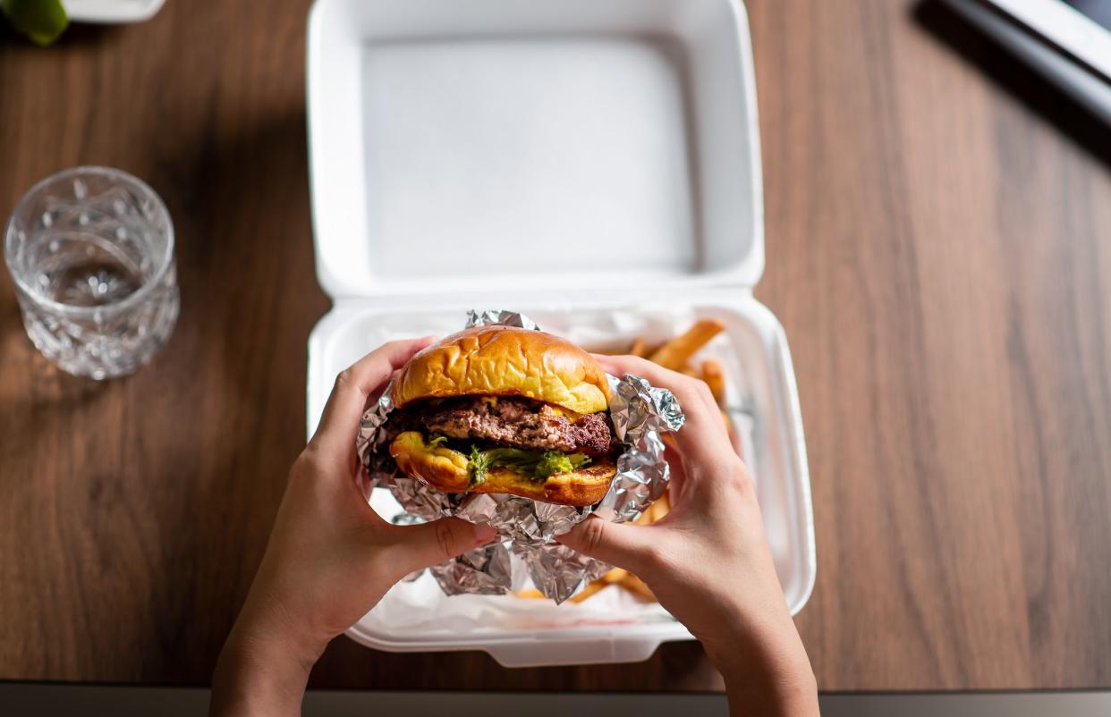 Woman eating fast food meal of burger and fries delivered at home first person view