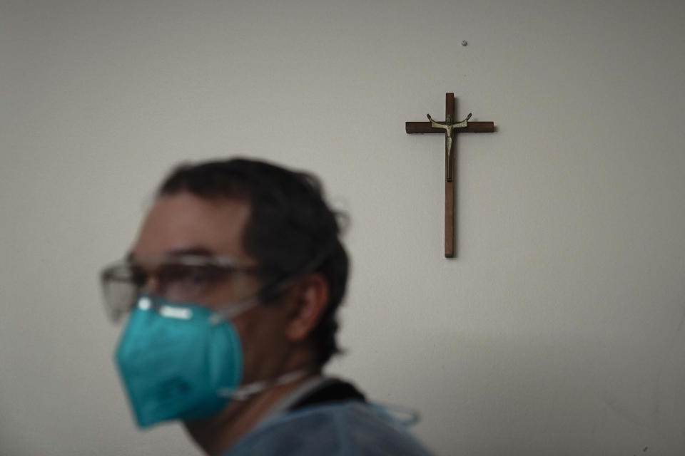 Chaplain Kevin Deegan walks past a crucifix in a COVID-19 unit at Providence Holy Cross Medical Center in the Mission Hills section of Los Angeles on Saturday, Jan. 9, 2021. Deegan's job, and that of his fellow chaplains at the 377-bed medical center, is to minister to every one of them and also their loved ones. So each day for the past 11 months he has been entering the rooms of the sick and dying clad in a face mask, face shield, gloves and full body cover to pray with them, hold their hands, gently brush their foreheads and reassure them there is nothing to fear. (AP Photo/Jae C. Hong)