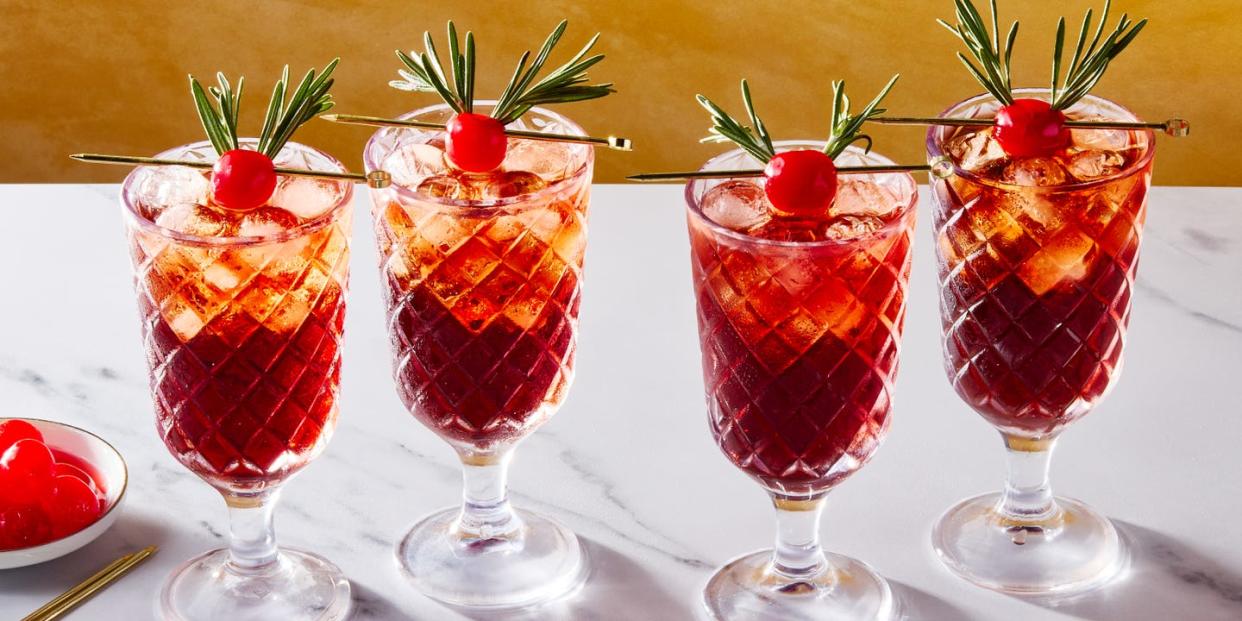 two glasses filled with ice, rum, cherry juice, and cola, garnished with a maraschino cherry decorated with two sprigs of rosemary